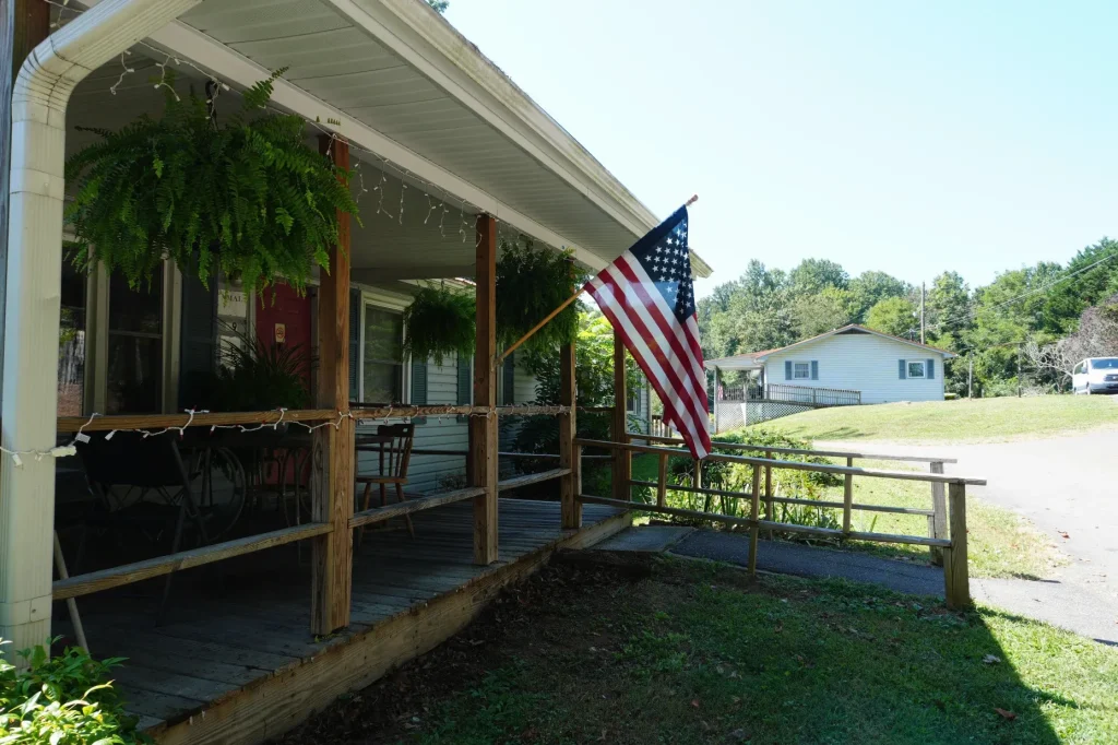 Looking down the front porch past the flag, with a second house visible across the drive.