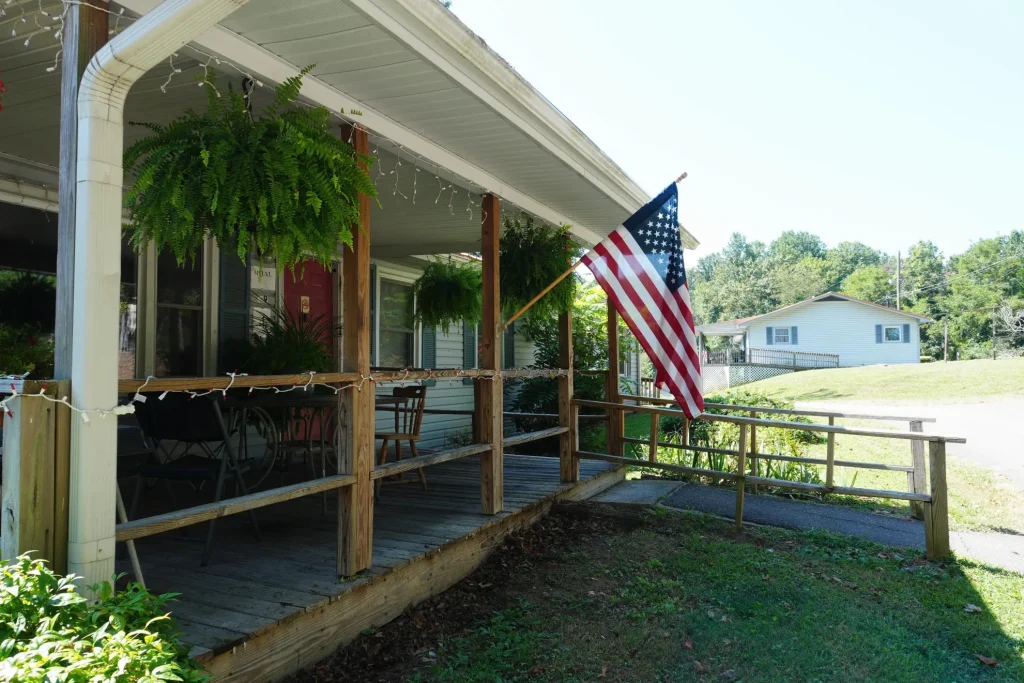 The full length of the covered porch, ferns hanging from the beam.