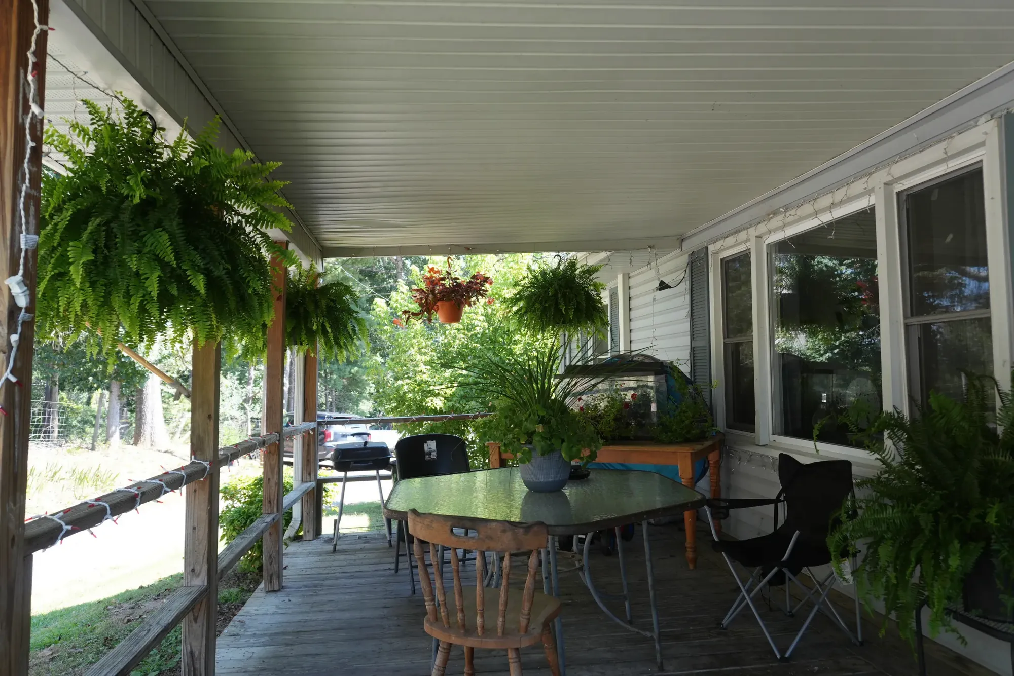 A table and chairs set out along the covered porch, under hanging baskets of ferns.