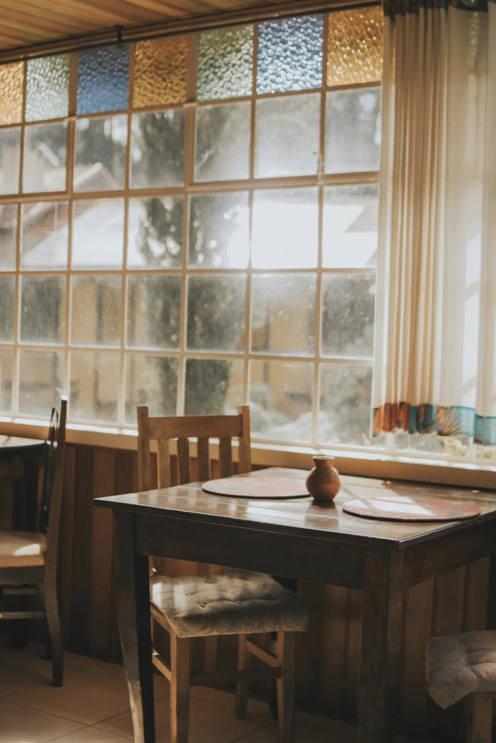 A wooden table and chairs beside a large window in a home dining room.