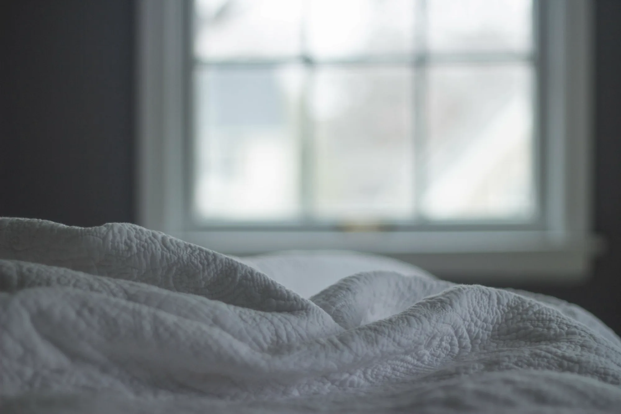 A quilted blanket folded on a bed beside a window in morning light.