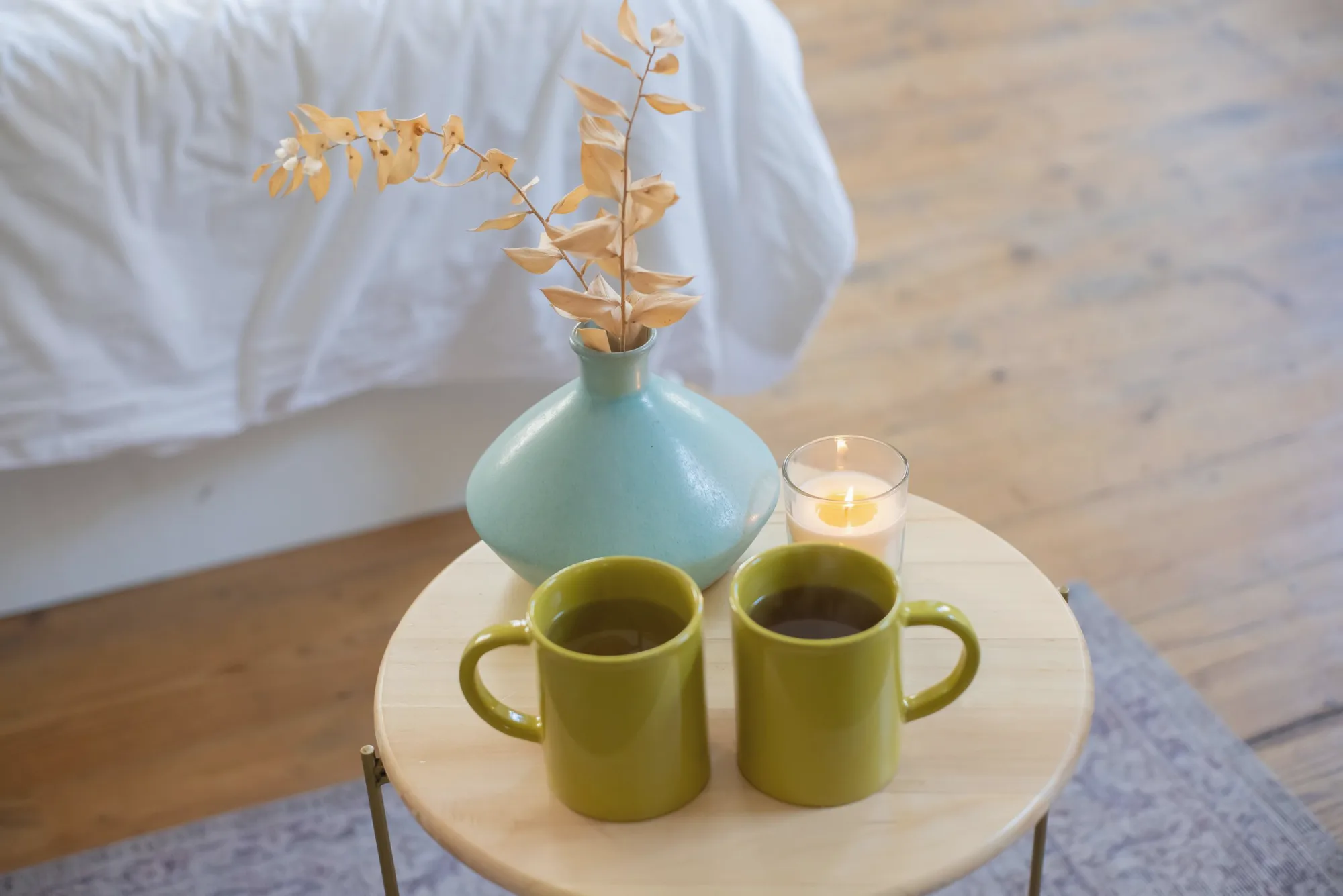 Two mugs of tea on a small table beside a vase and a lit candle.